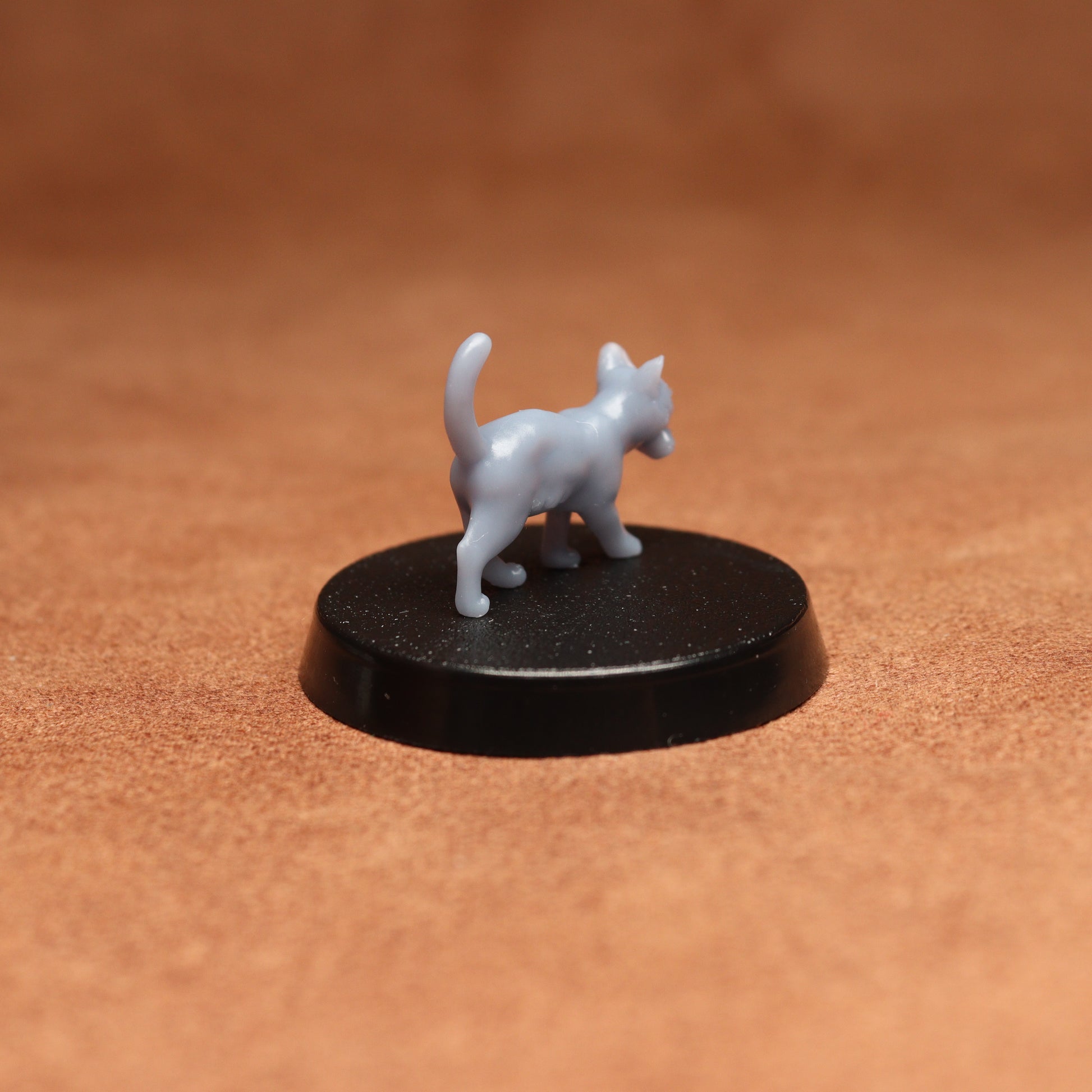 Small white cat figurine on a black base against a brown background