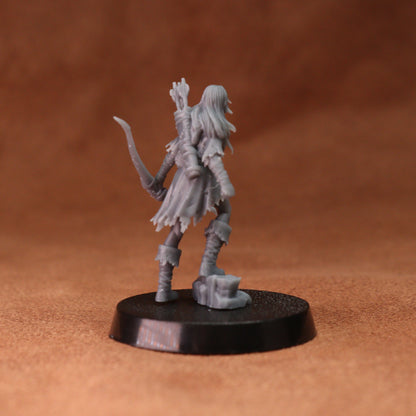 A gray unpainted fantasy miniature figurine of a female archer standing on a round black base, photographed against a warm brown textured background.