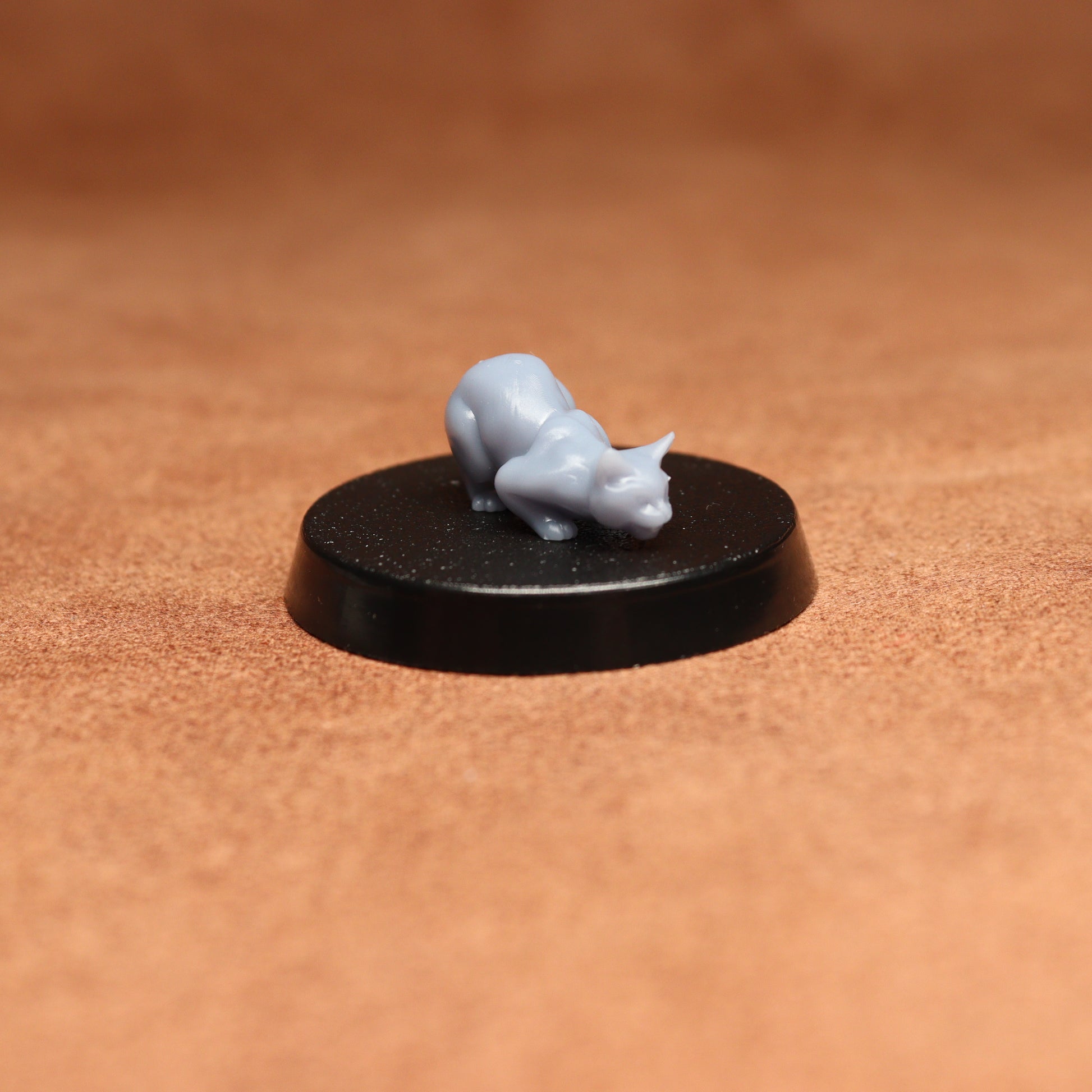 Small gray figurine on a black round base against a brown background