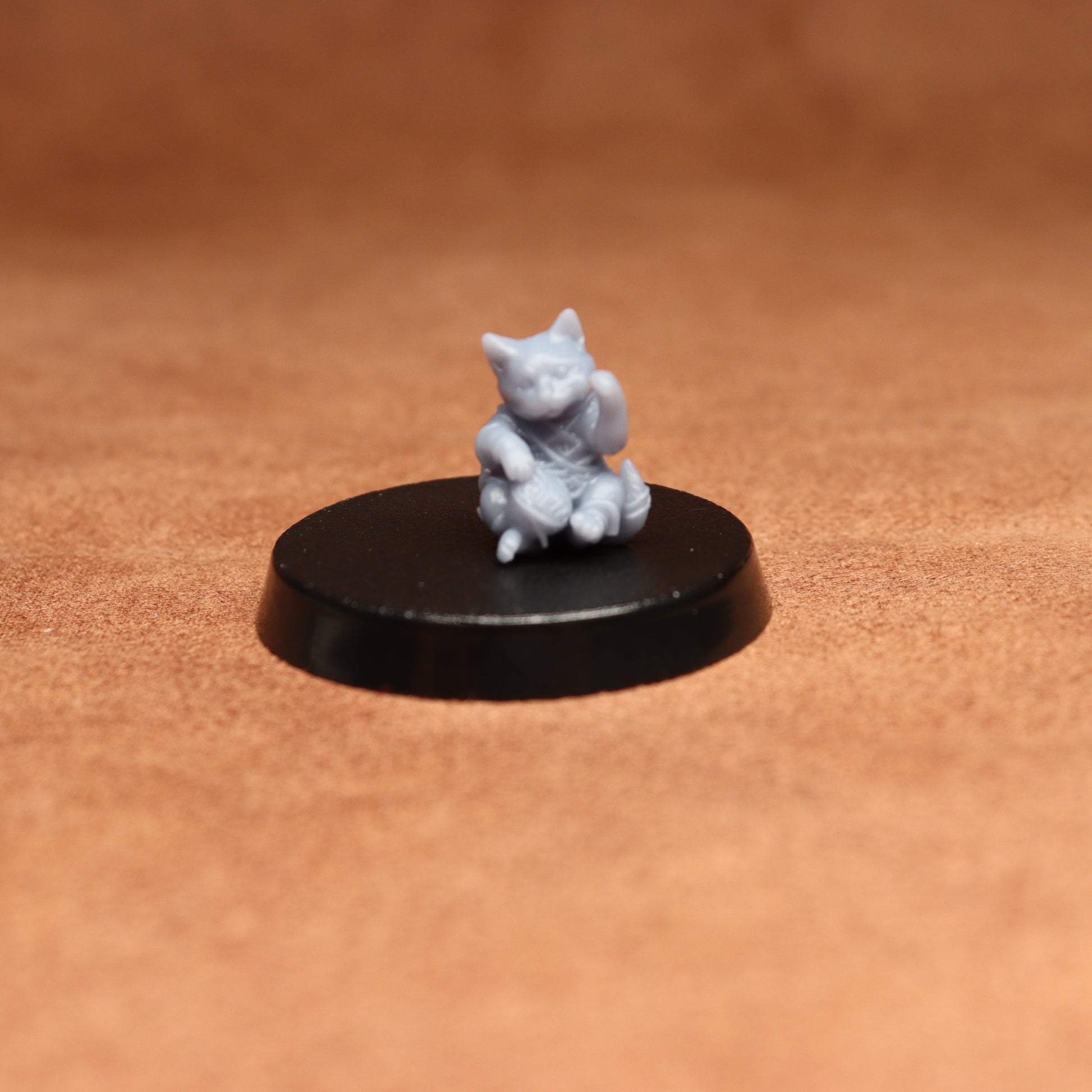 grey resin miniature cat figure on a black base with a brown background