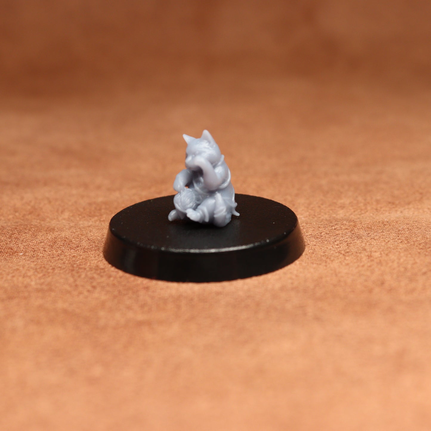 grey resin miniature cat figure on a black base with a brown background