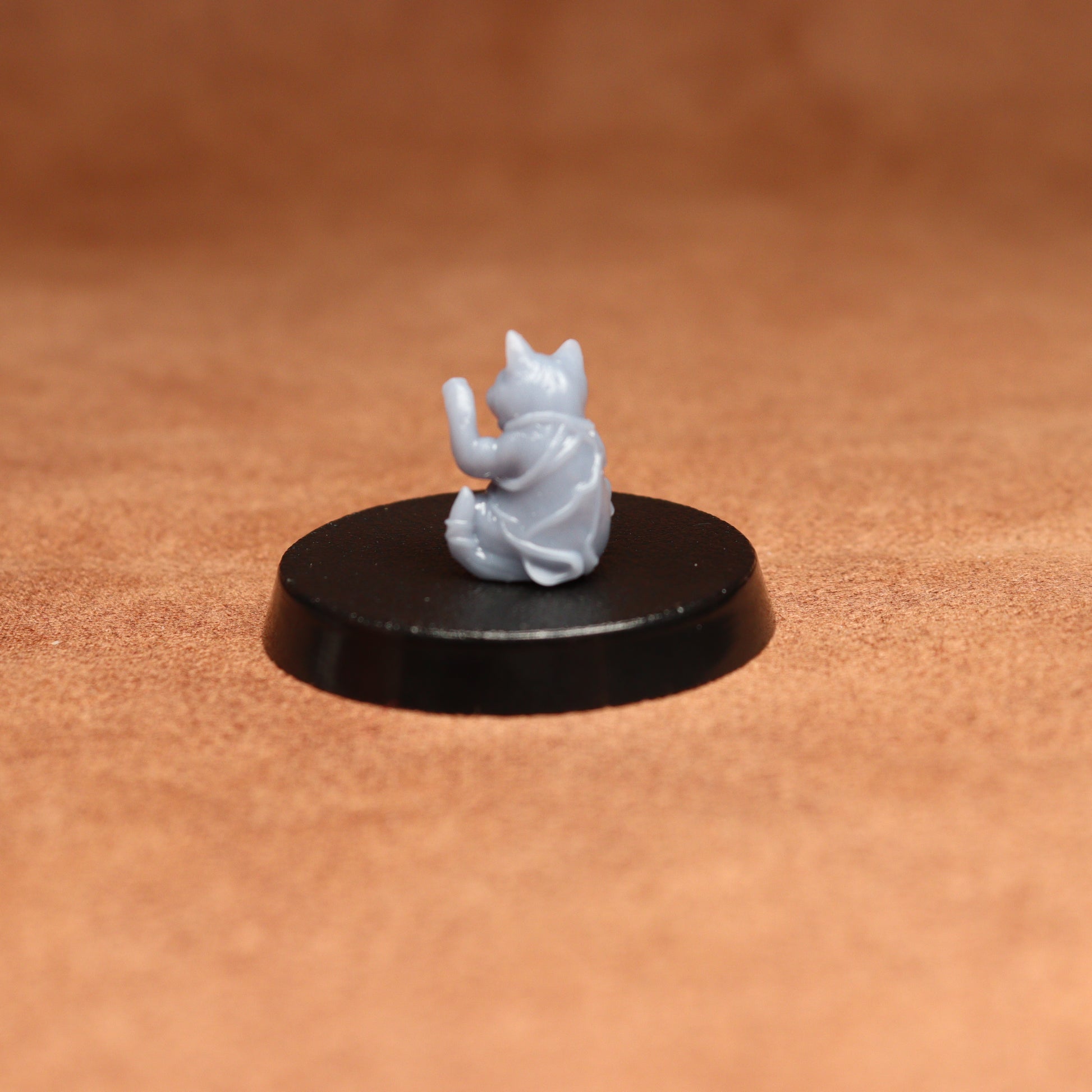 grey resin miniature cat figure on a black base with a brown background