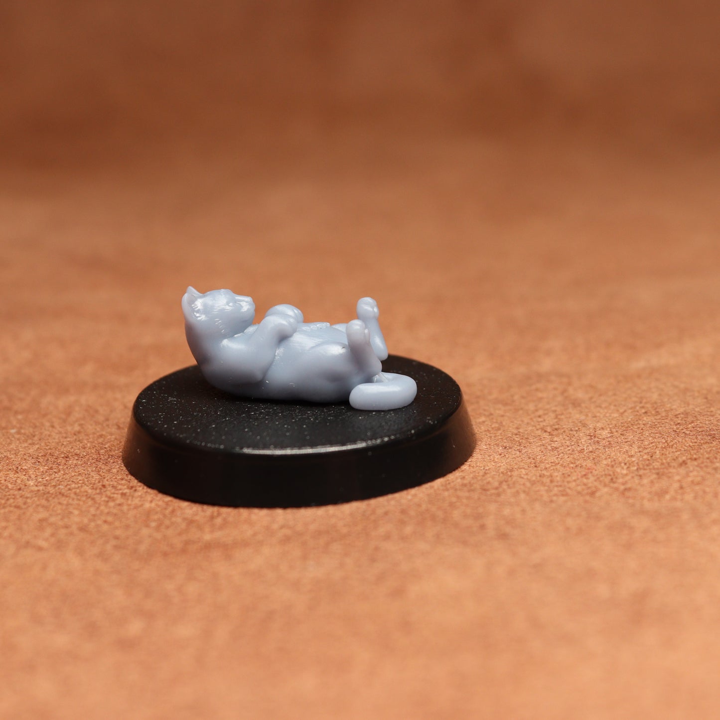grey cat resin miniature on a black base on a brown background.
