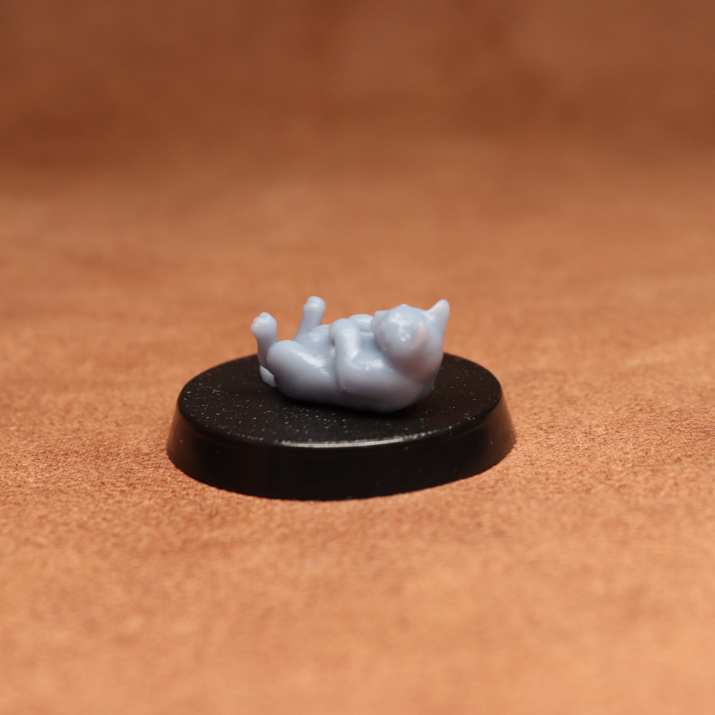 grey cat resin miniature on a black base on a brown background.