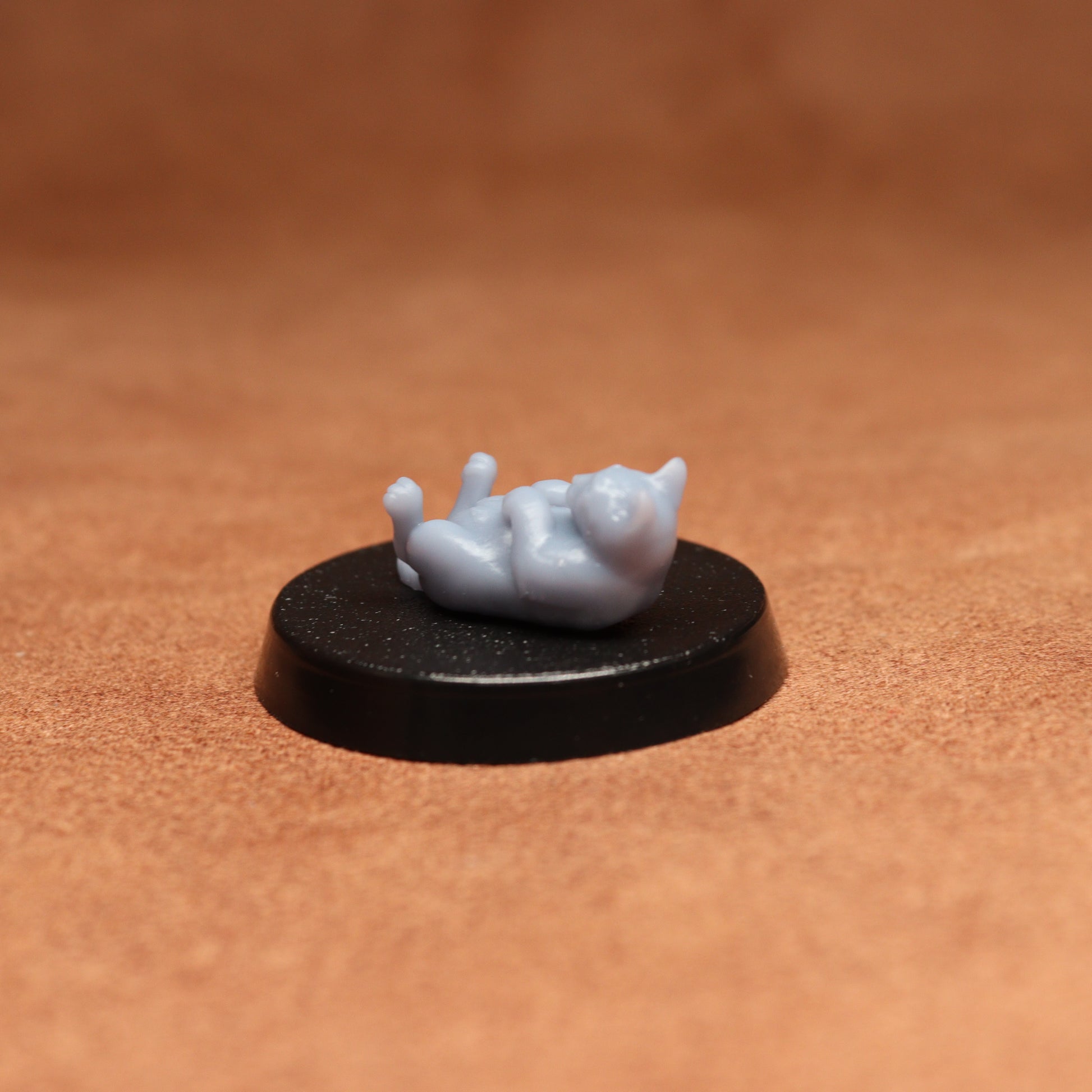 grey cat resin miniature on a black base on a brown background.
