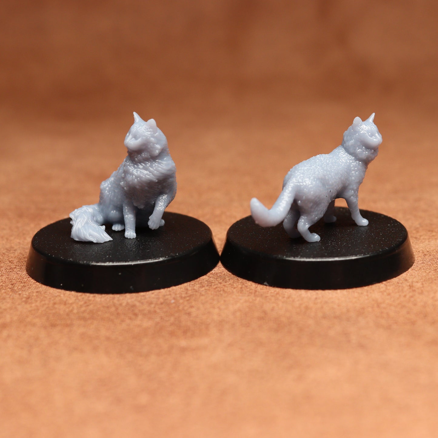 Two miniature cat figurines on black bases against a brown background