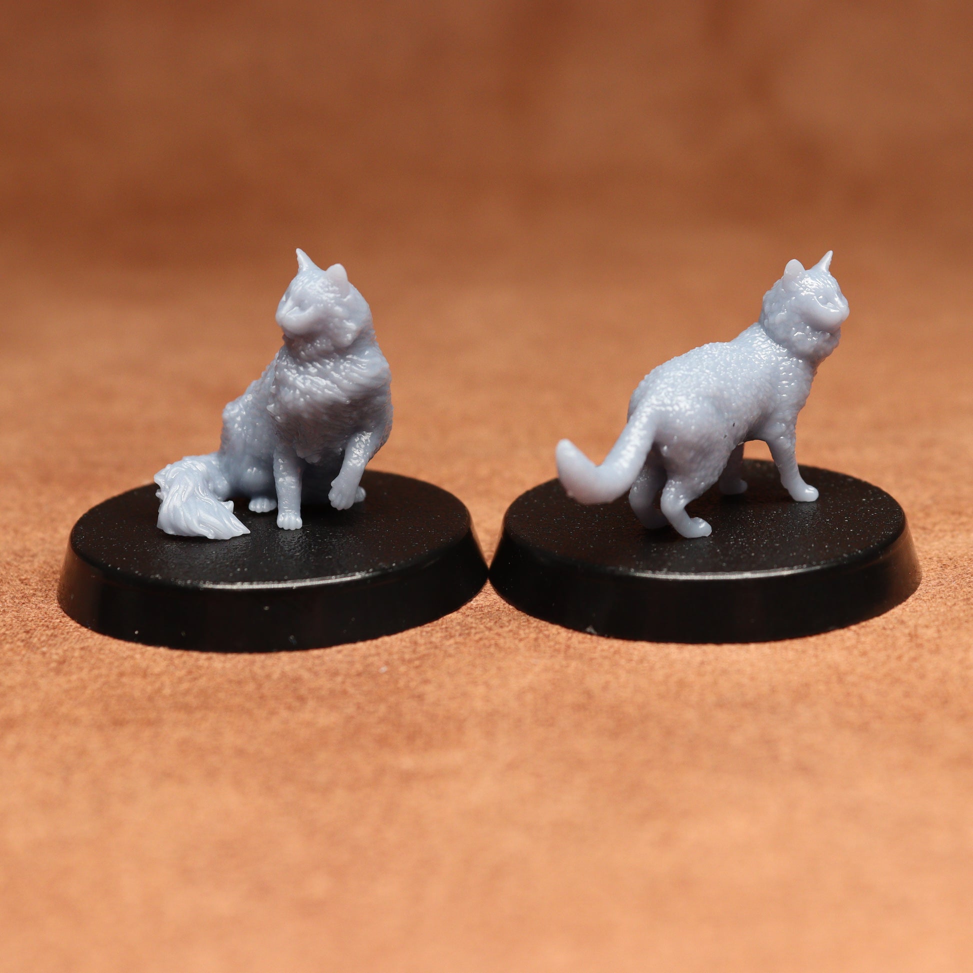 Two miniature cat figurines on black bases against a brown background