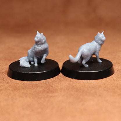 Two miniature cat figurines on black bases against a brown background