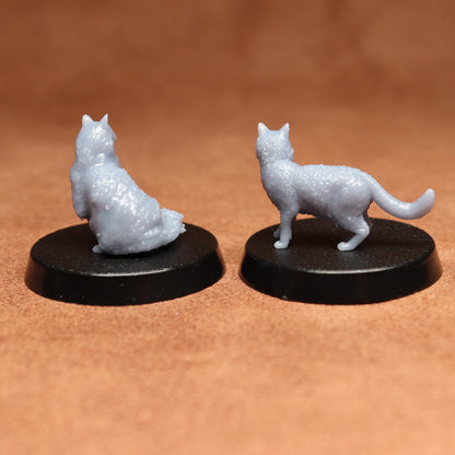 Two miniature cat figurines on black bases against a brown background