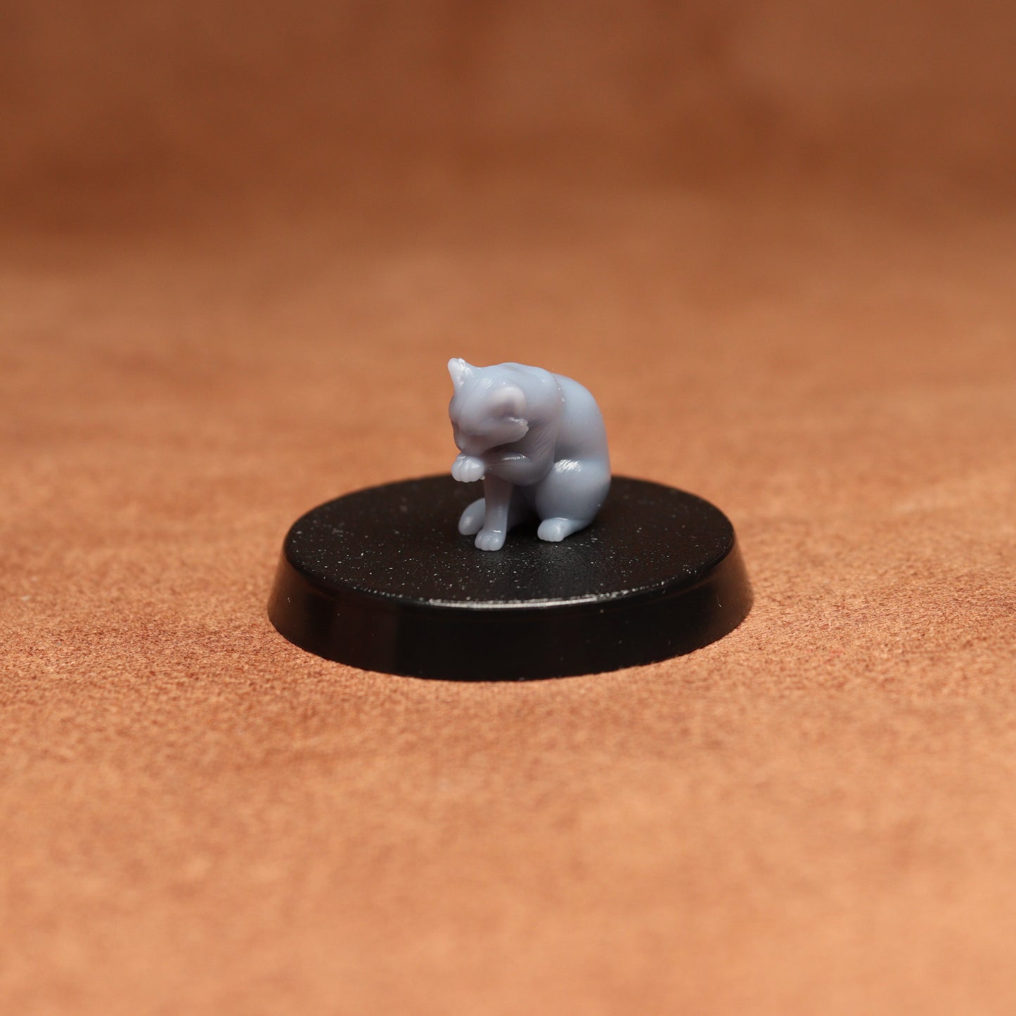 grey cat resin miniature on a black base on a brown background.