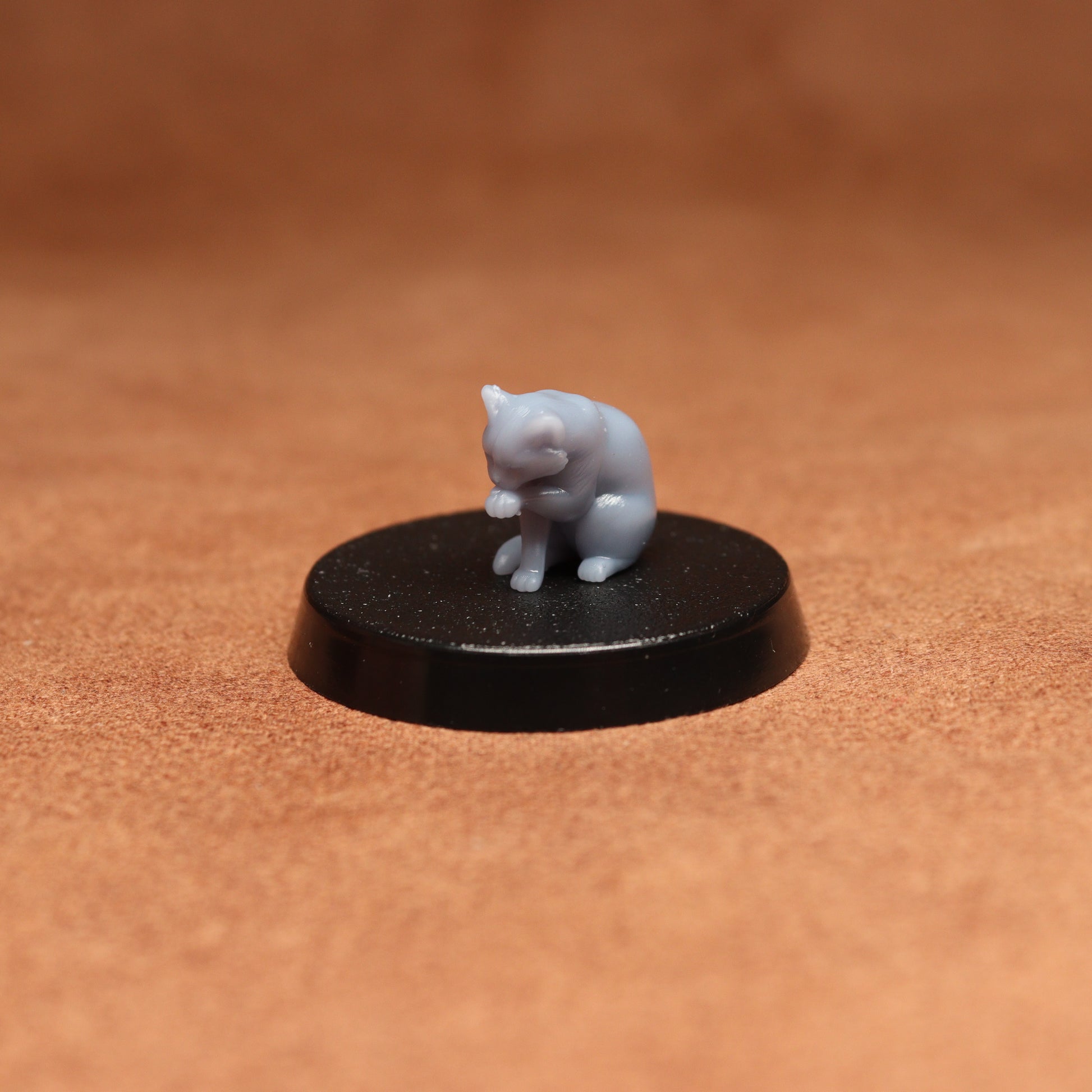 grey cat resin miniature on a black base on a brown background.