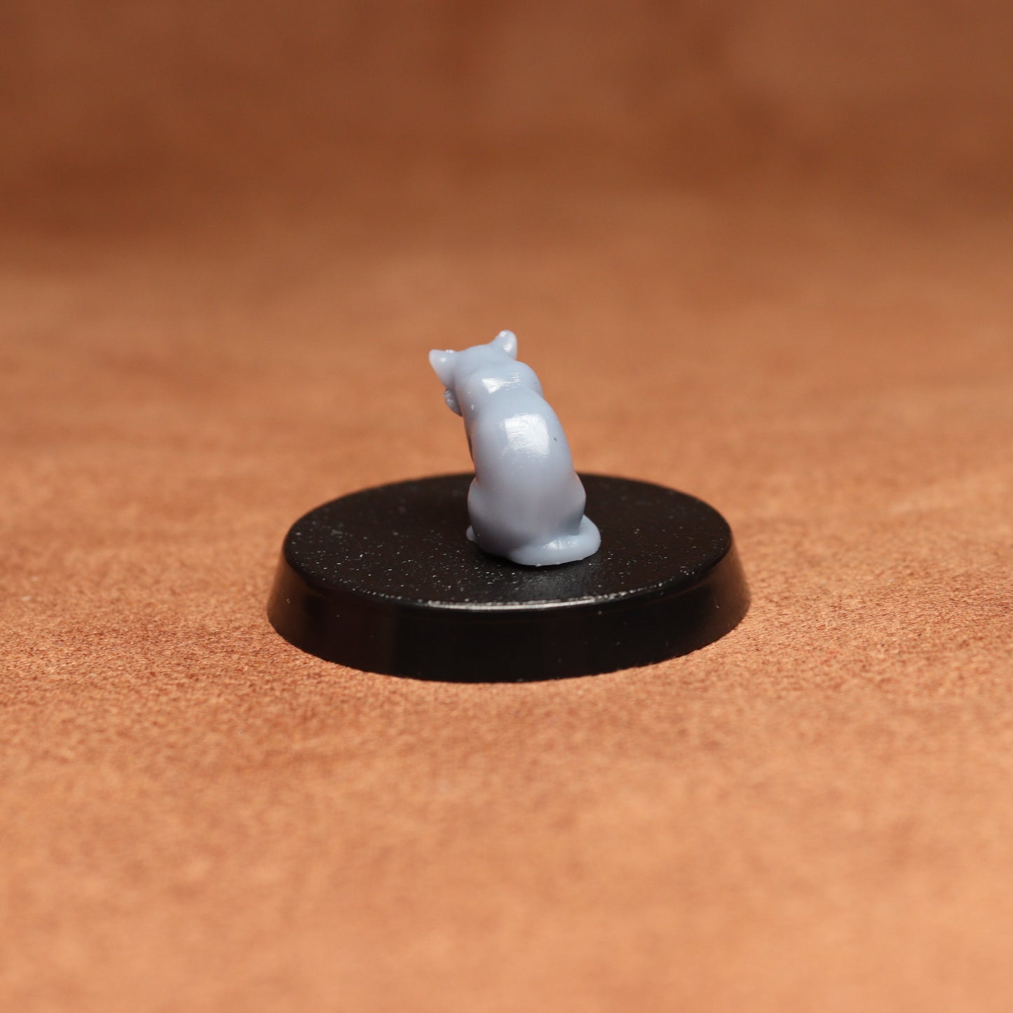 grey cat resin miniature on a black base on a brown background.