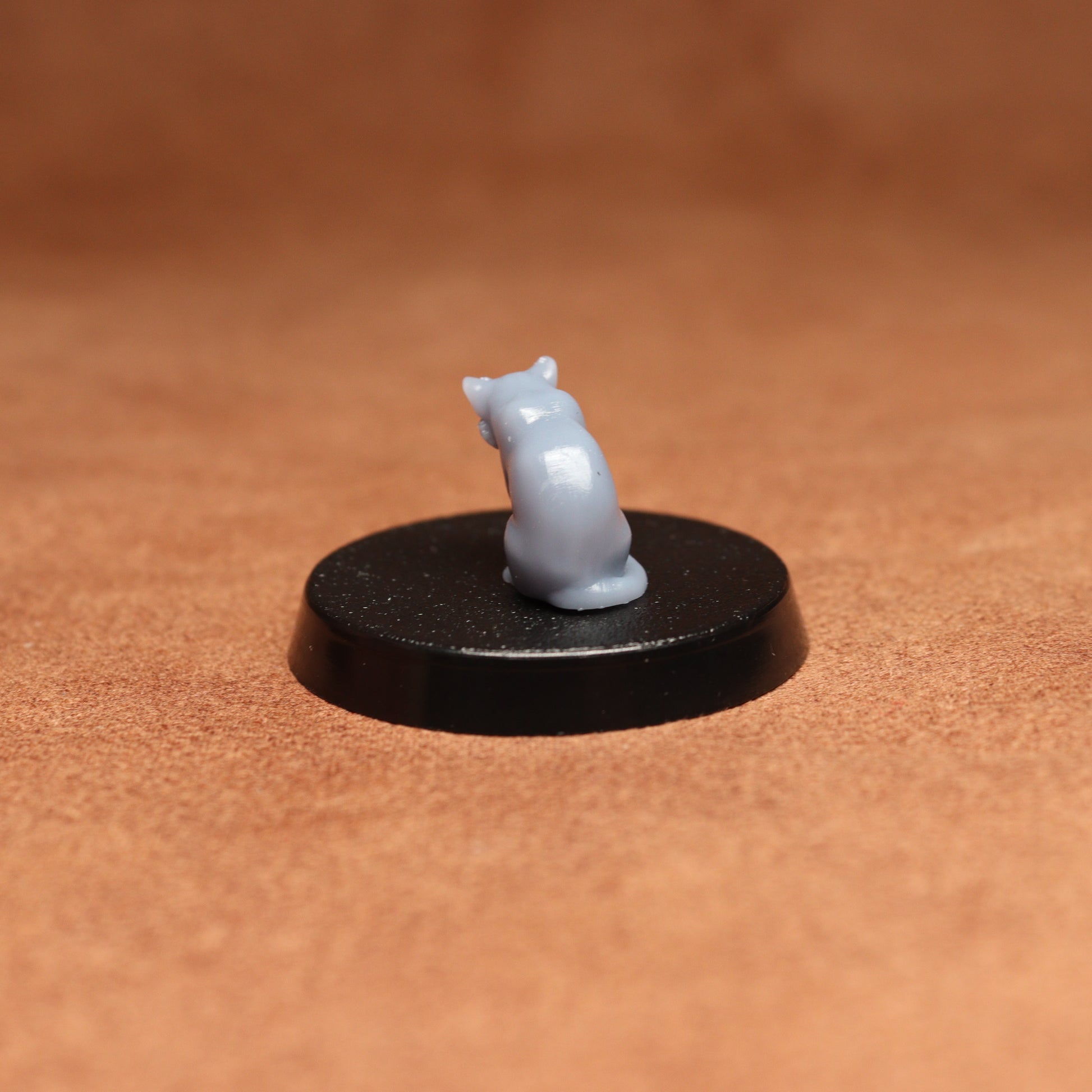 grey cat resin miniature on a black base on a brown background.