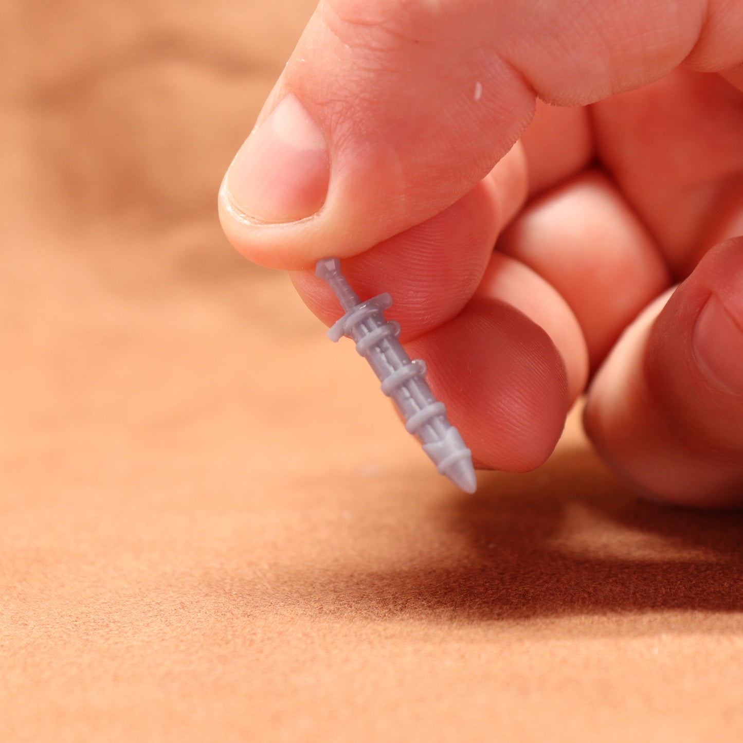 Hand holding a small gray screw against a blurred brown background