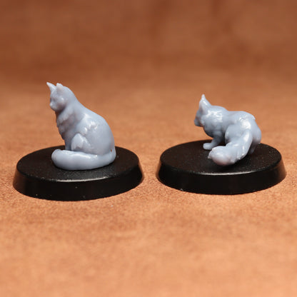 Two miniature cat figurines on black bases against a brown background