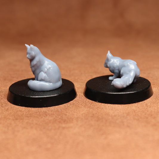 Two miniature cat figurines on black bases against a brown background