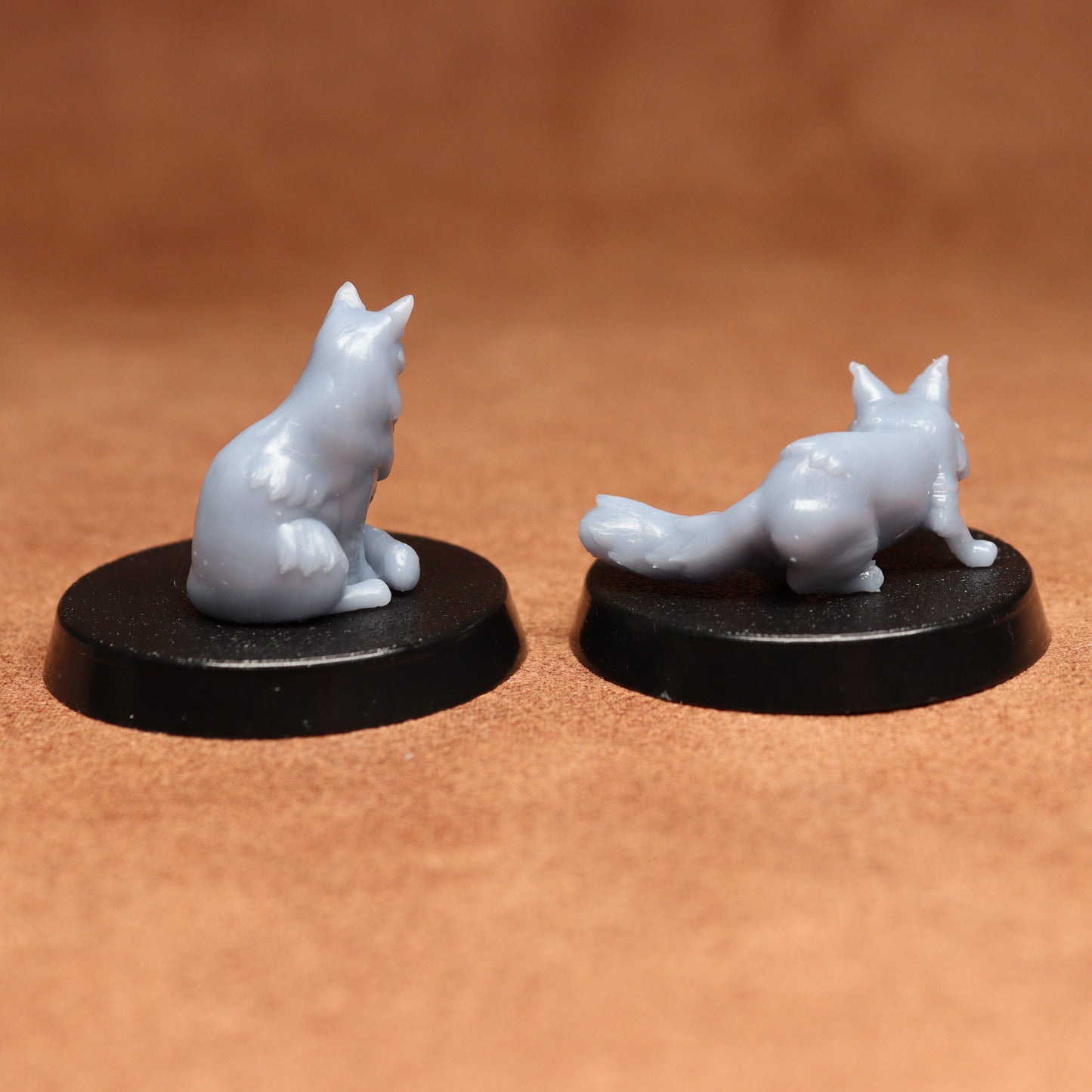 Two gray cat figurines on black bases against a brown background