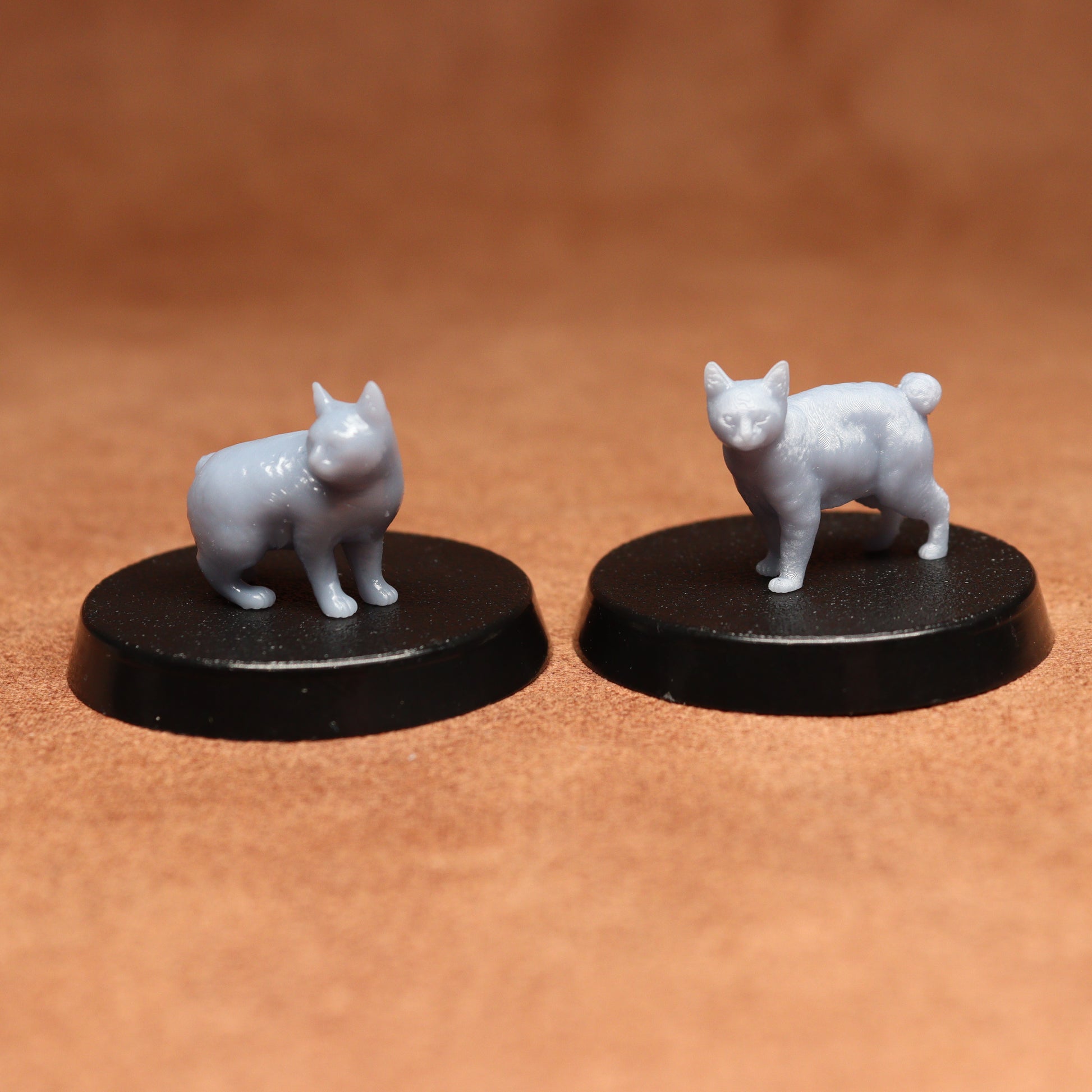 Two white cat figurines on black bases against a brown background