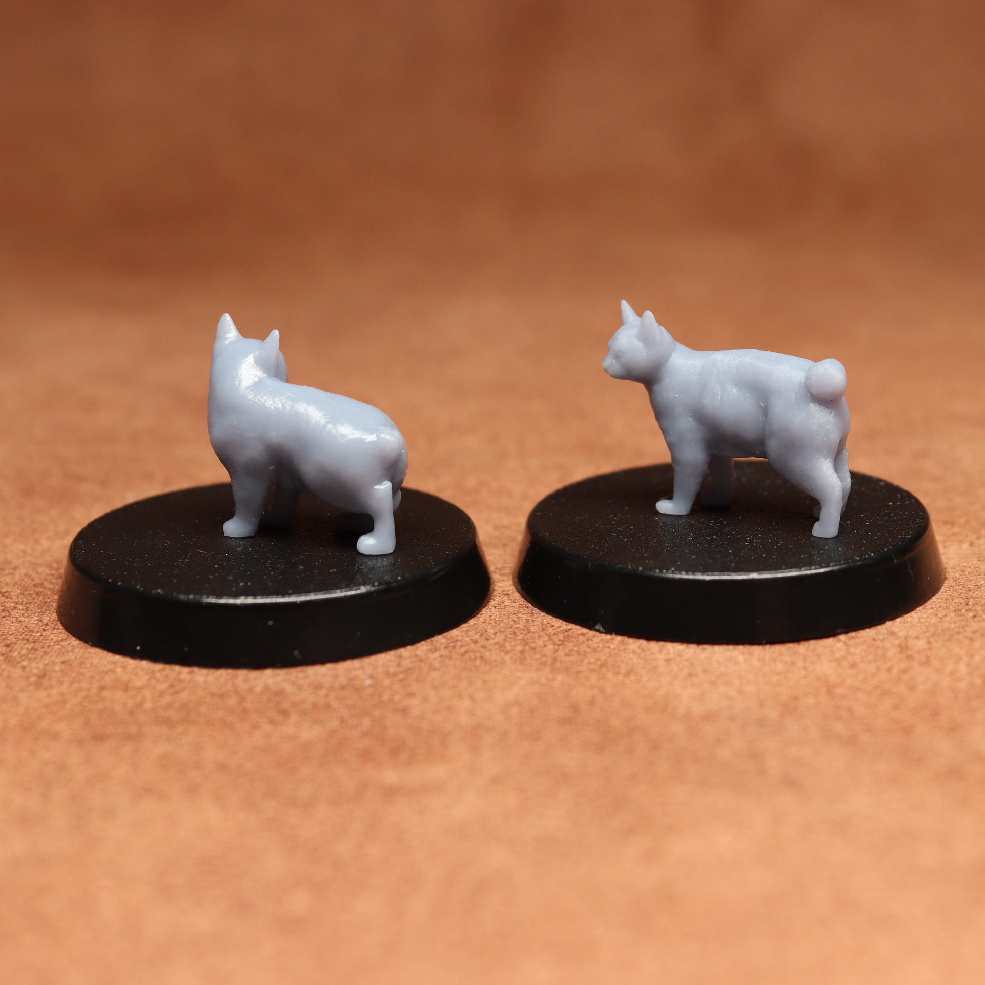 Two white cat figurines on black bases against a brown background
