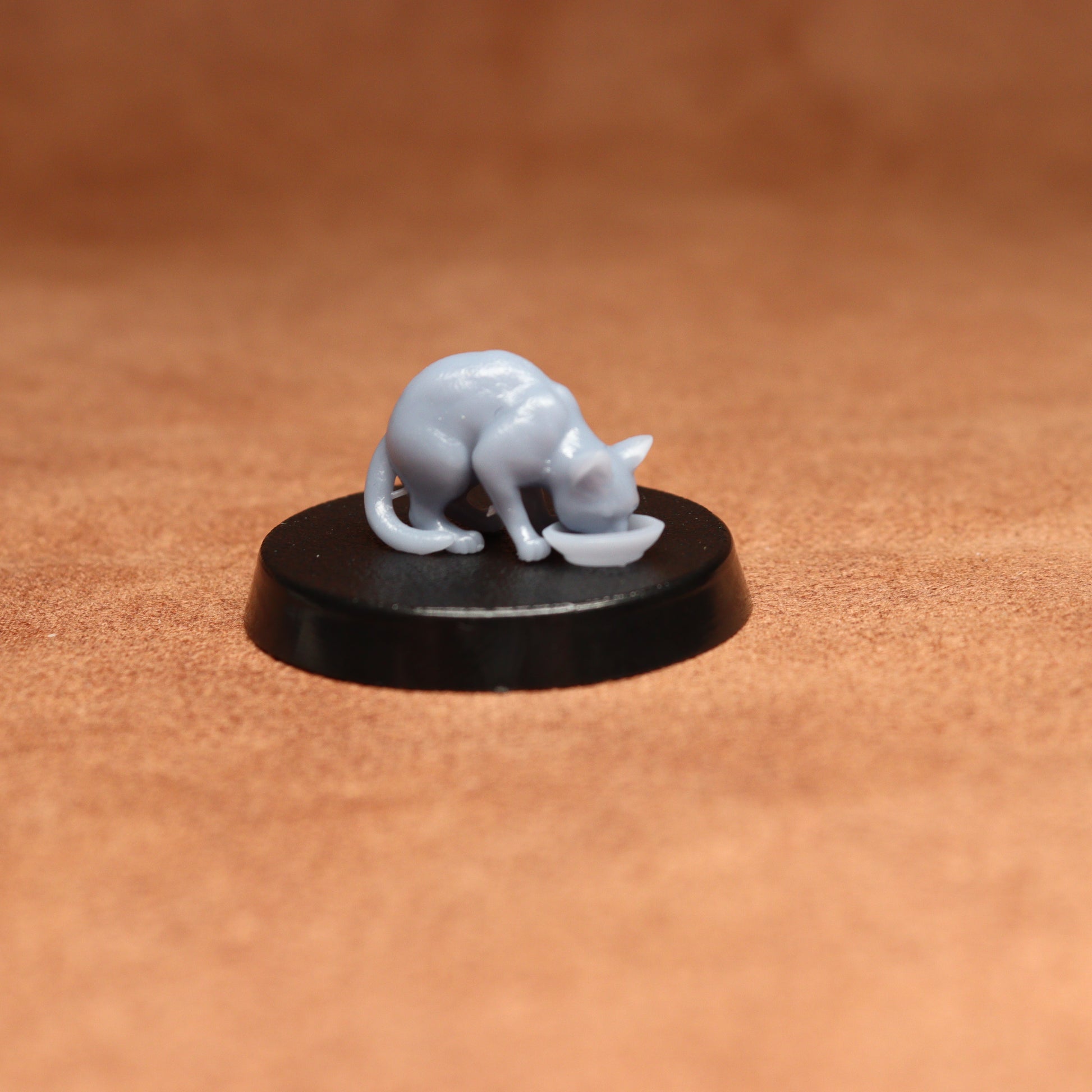 grey resin miniature cat figure on a black base with a brown background