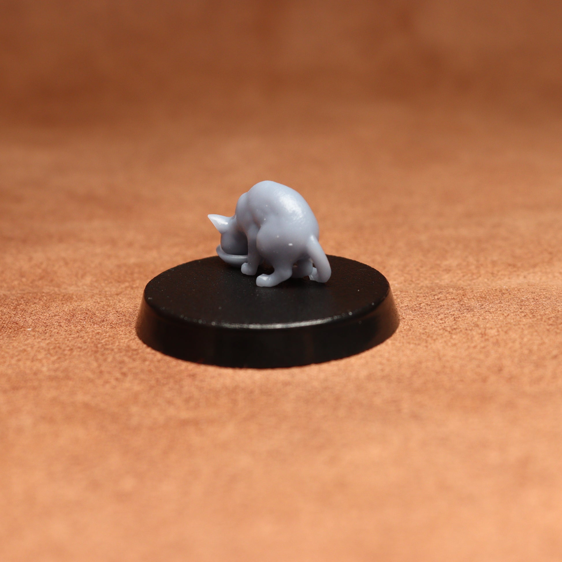 grey resin miniature cat figure on a black base with a brown background