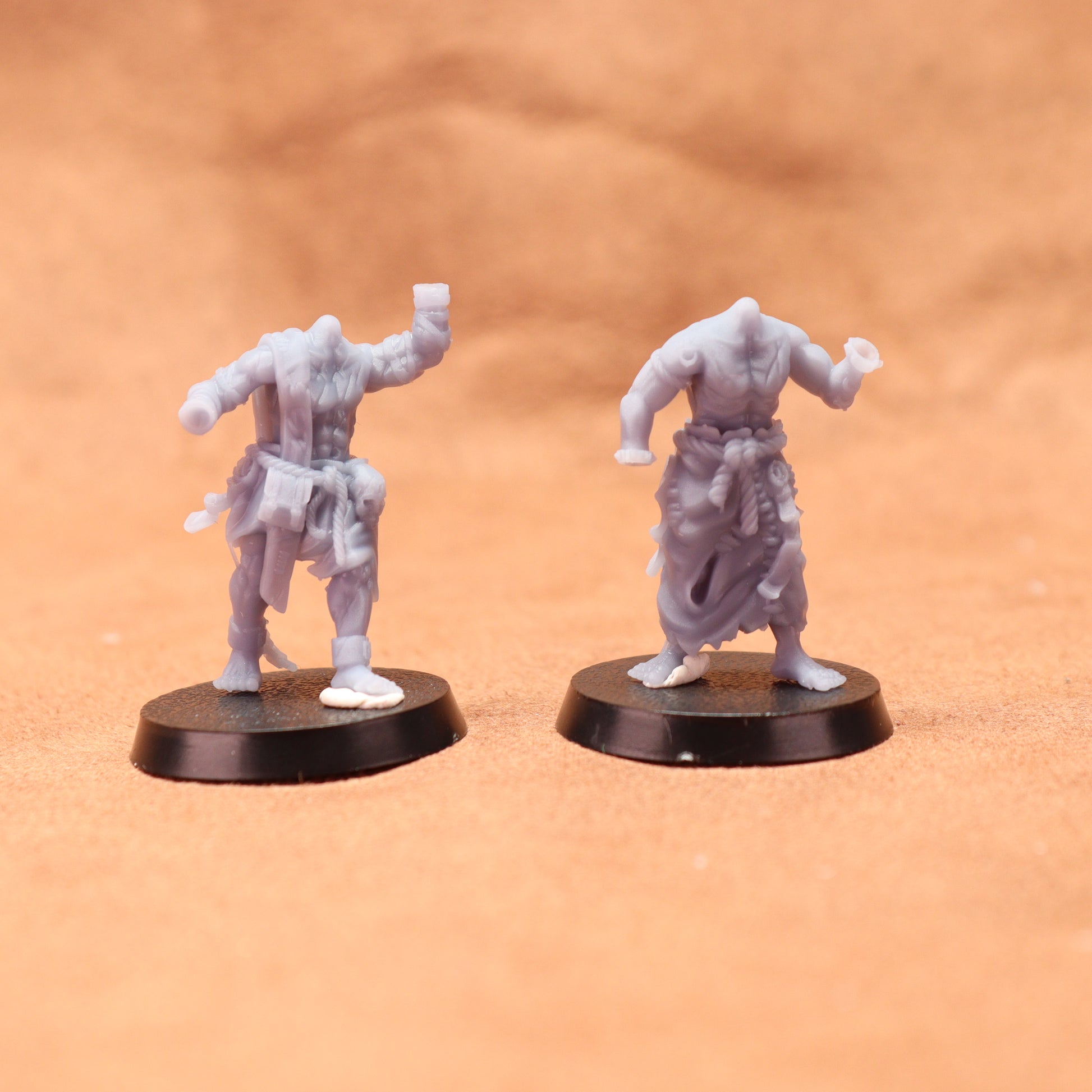 Two gray miniature figures on black bases against a brown background