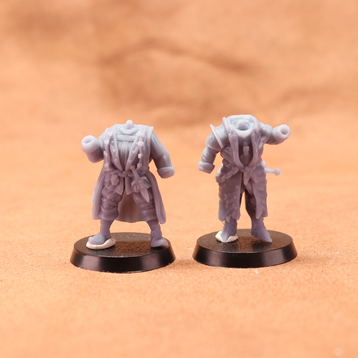 Two miniature figurines on round bases against a brown background
