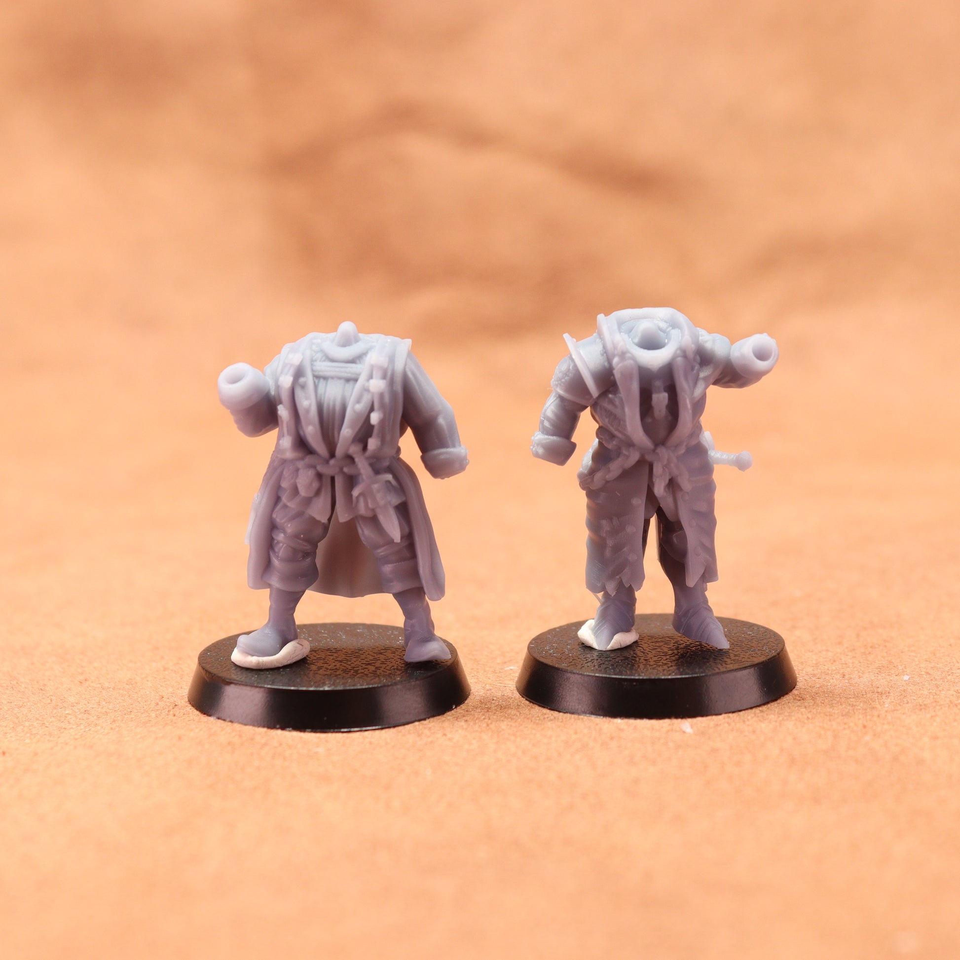 Two miniature figurines on round bases against a brown background