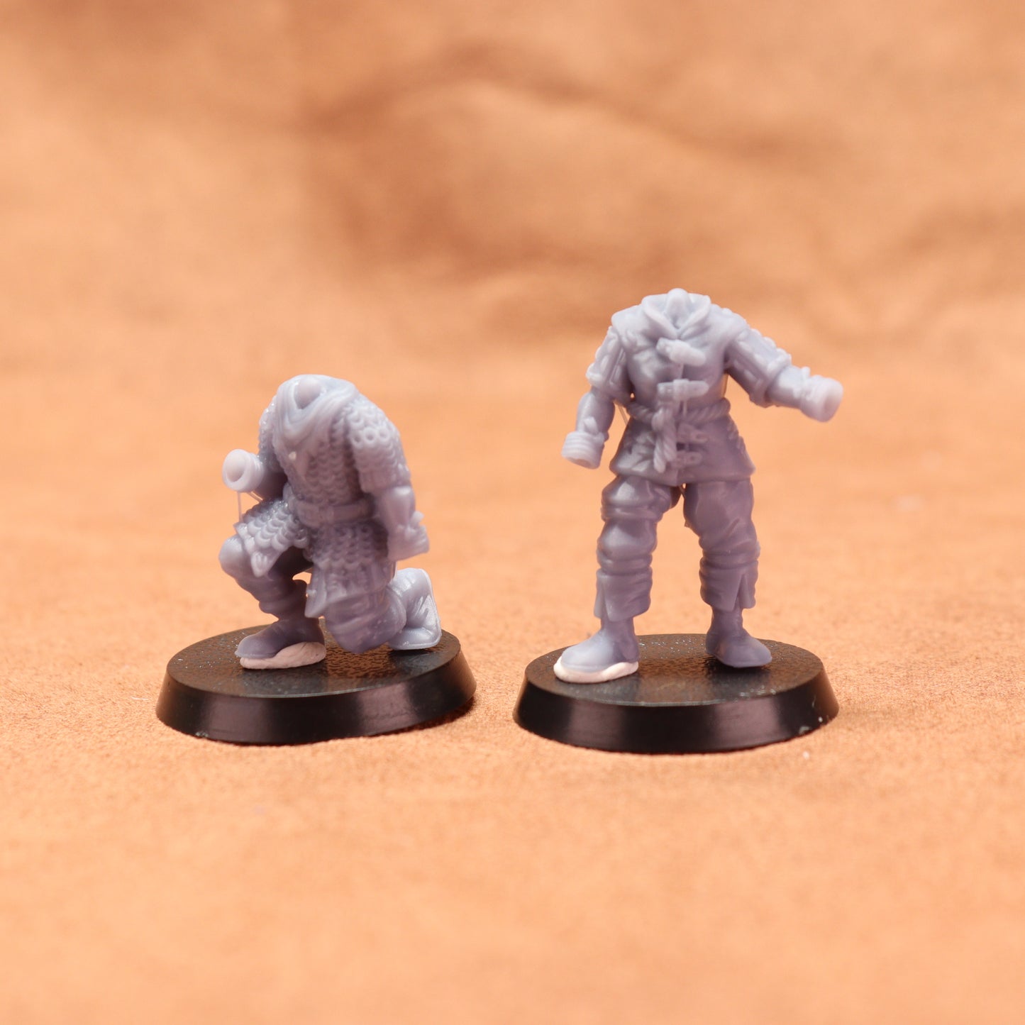Two miniature figures on black bases against a beige background