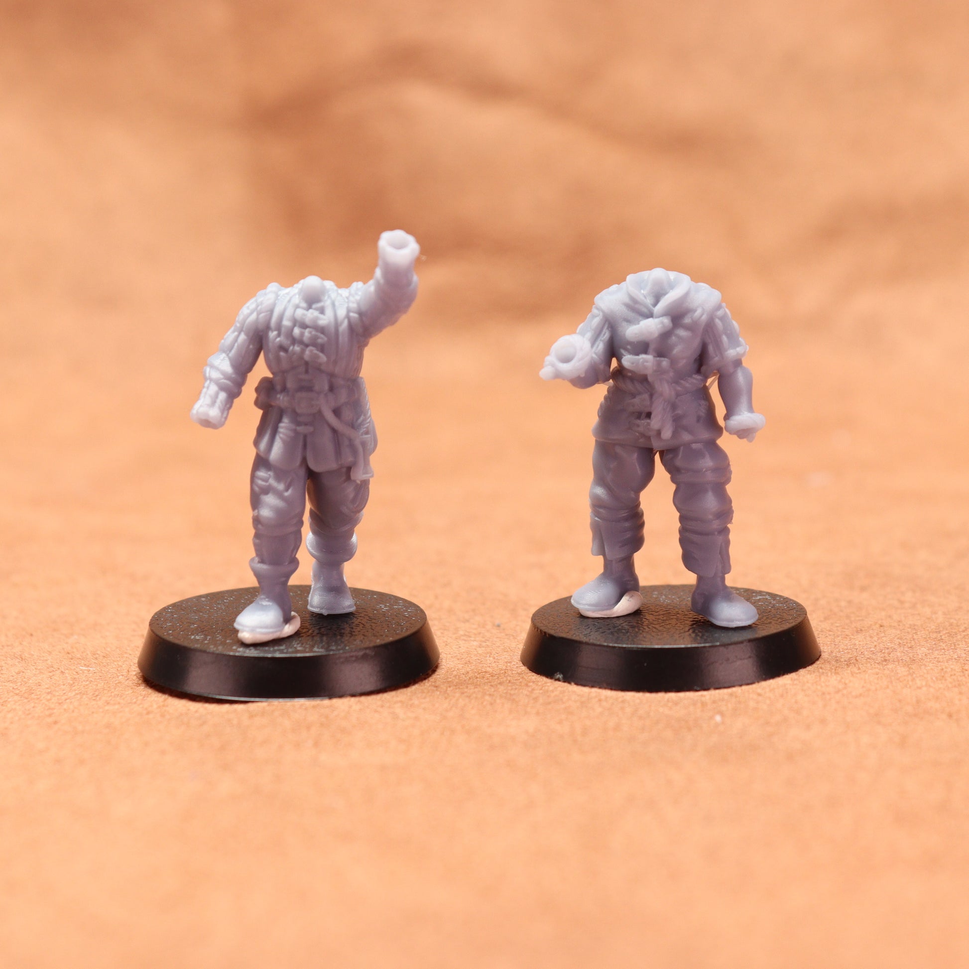 Two miniature figures on round bases against a brown background