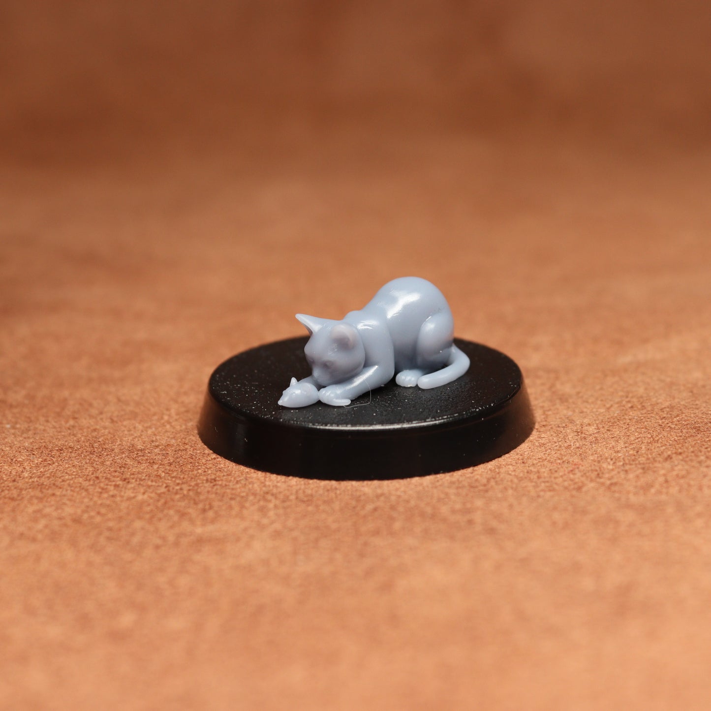 Small figurine of a cat on a round black base against a brown background