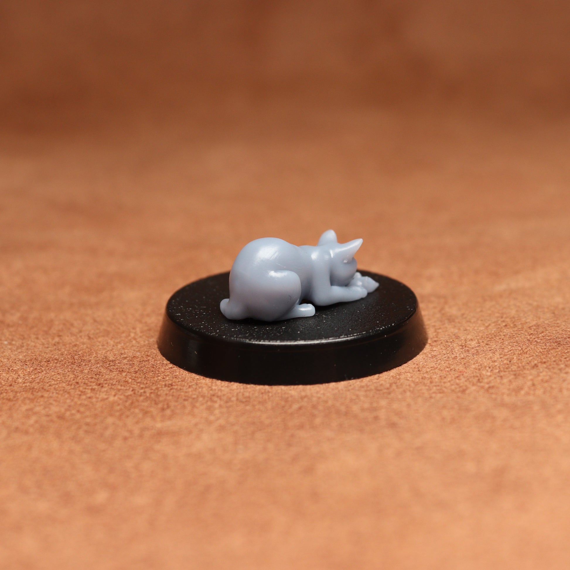 Small figurine of a cat on a black base against a brown background