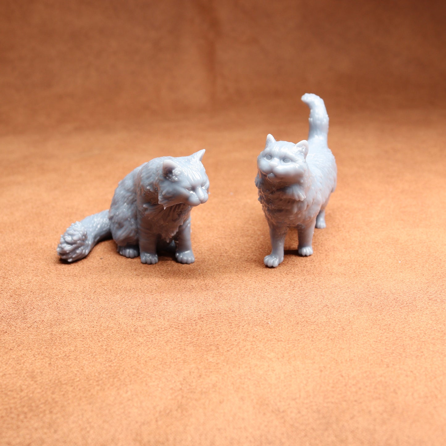 Two small cat figurines on a textured orange surface