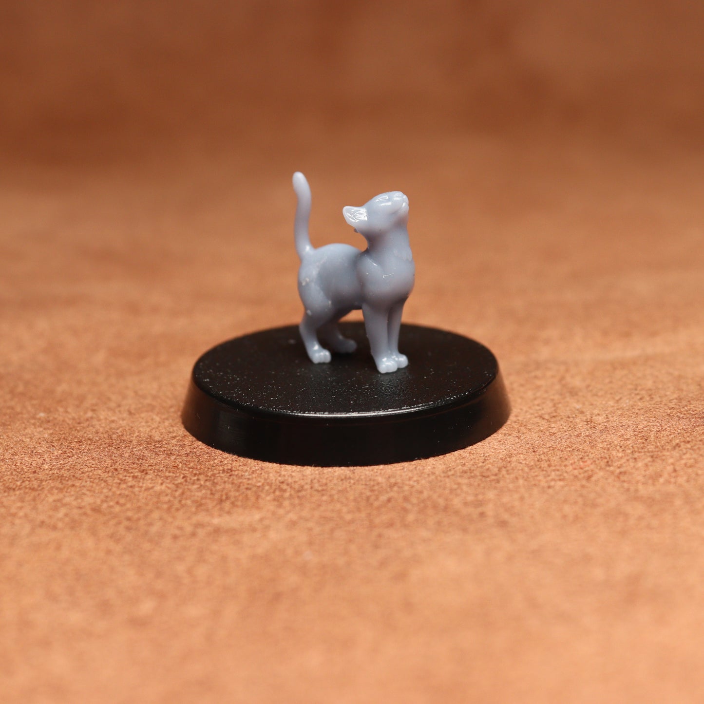 Small gray cat figurine on a black round base against a brown background