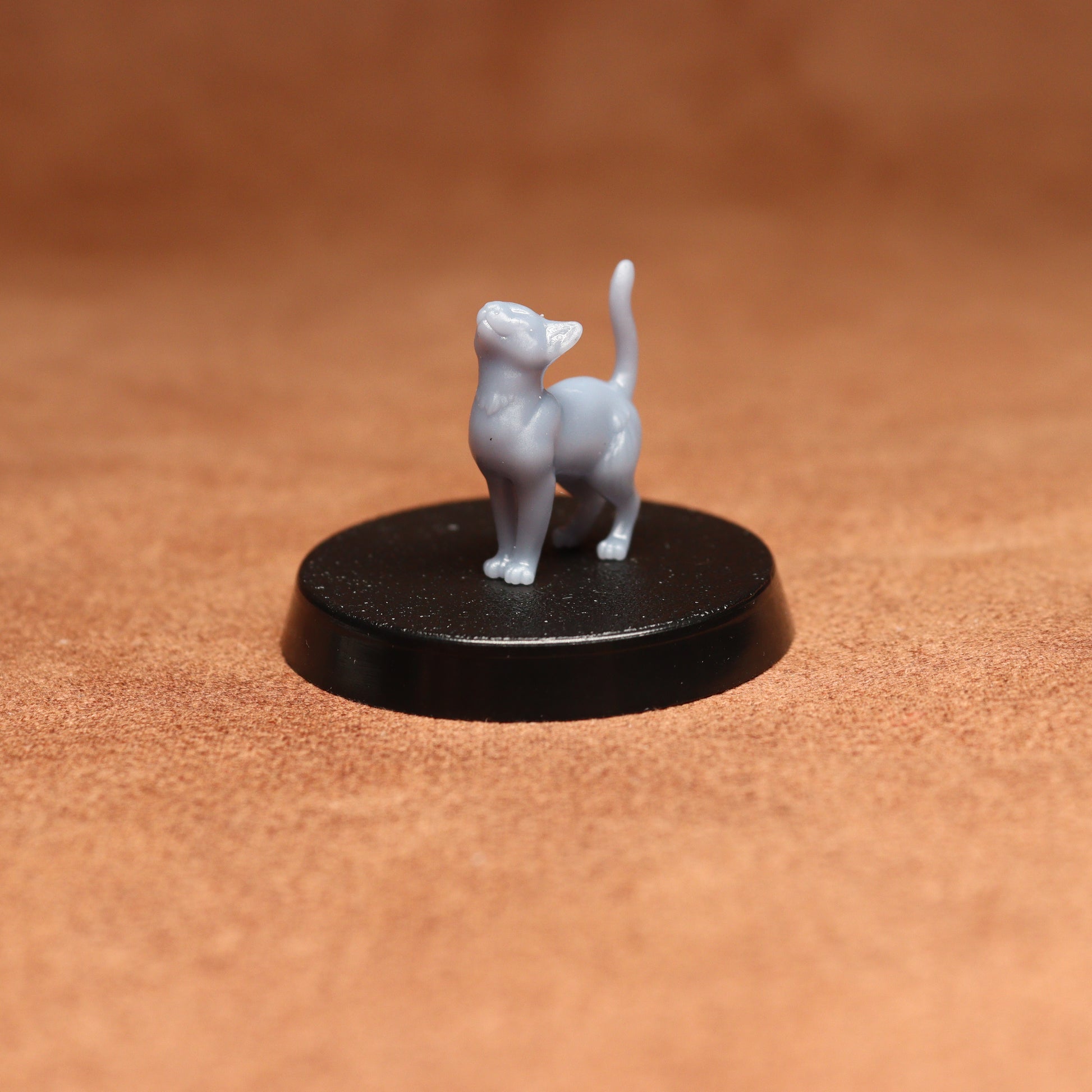 Small gray cat figurine on a black round base against a brown background
