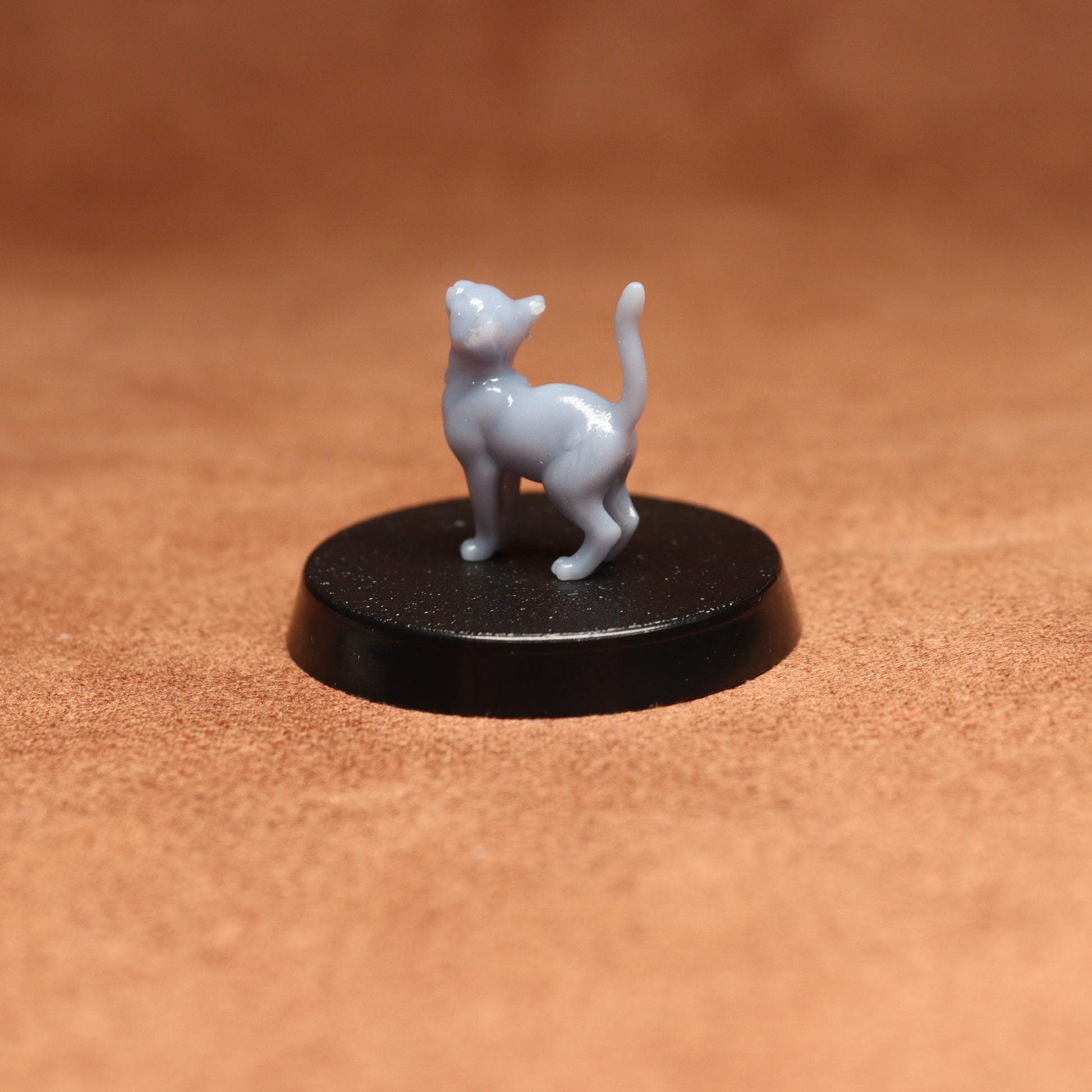 Small white cat figurine on a black round base against a brown background