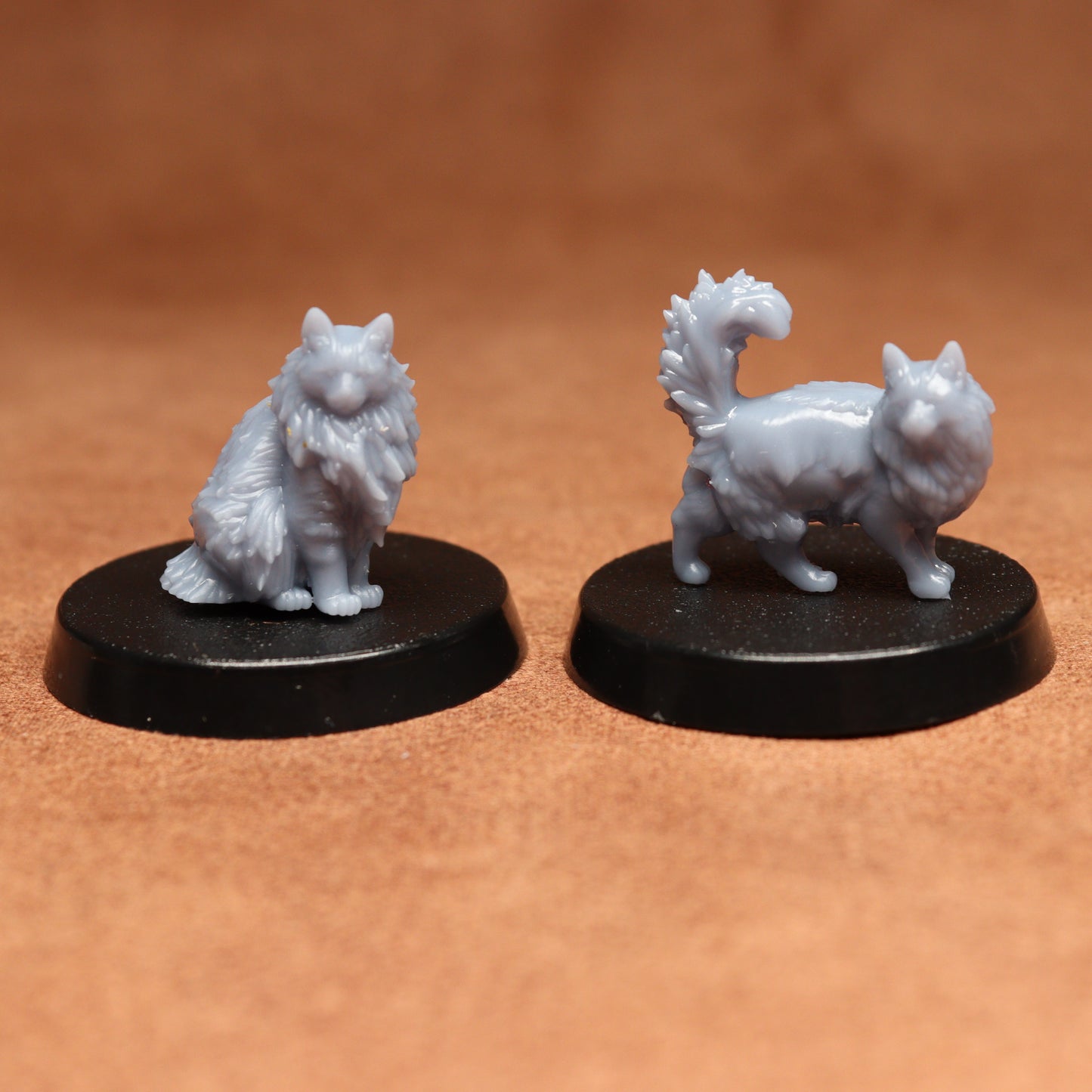 Two white fantasy cats figurines on black bases against a brown background