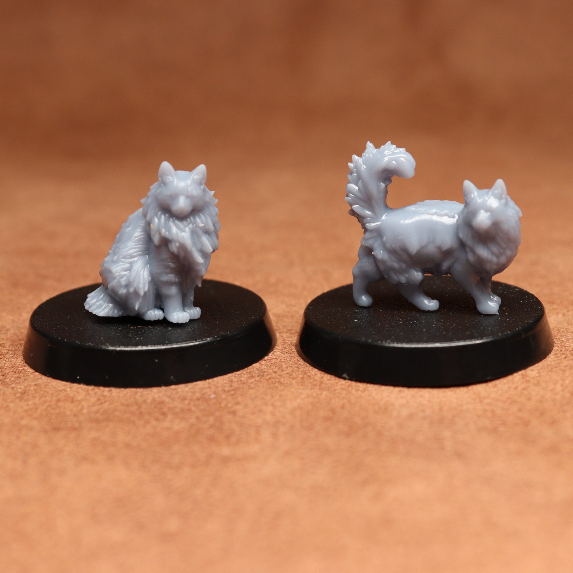 Two white fantasy cats figurines on black bases against a brown background