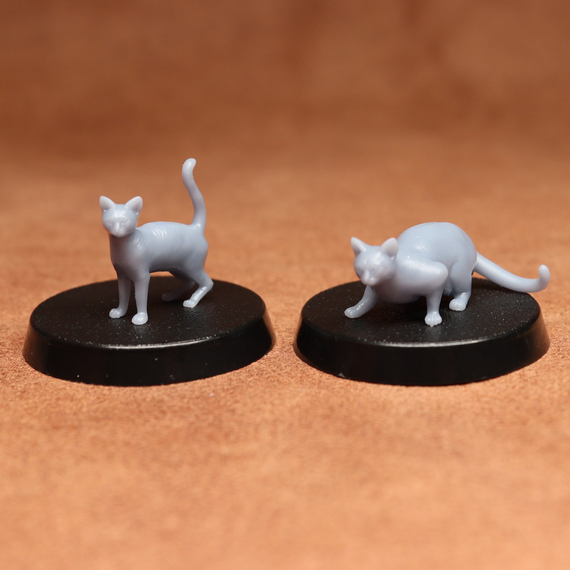 Two white cat figurines on black bases against a brown background