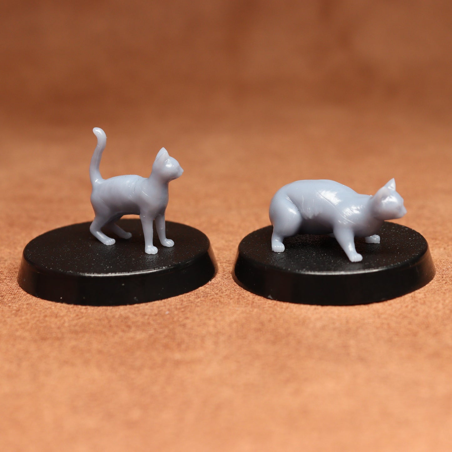 Two miniature cat figurines on black bases against a brown background