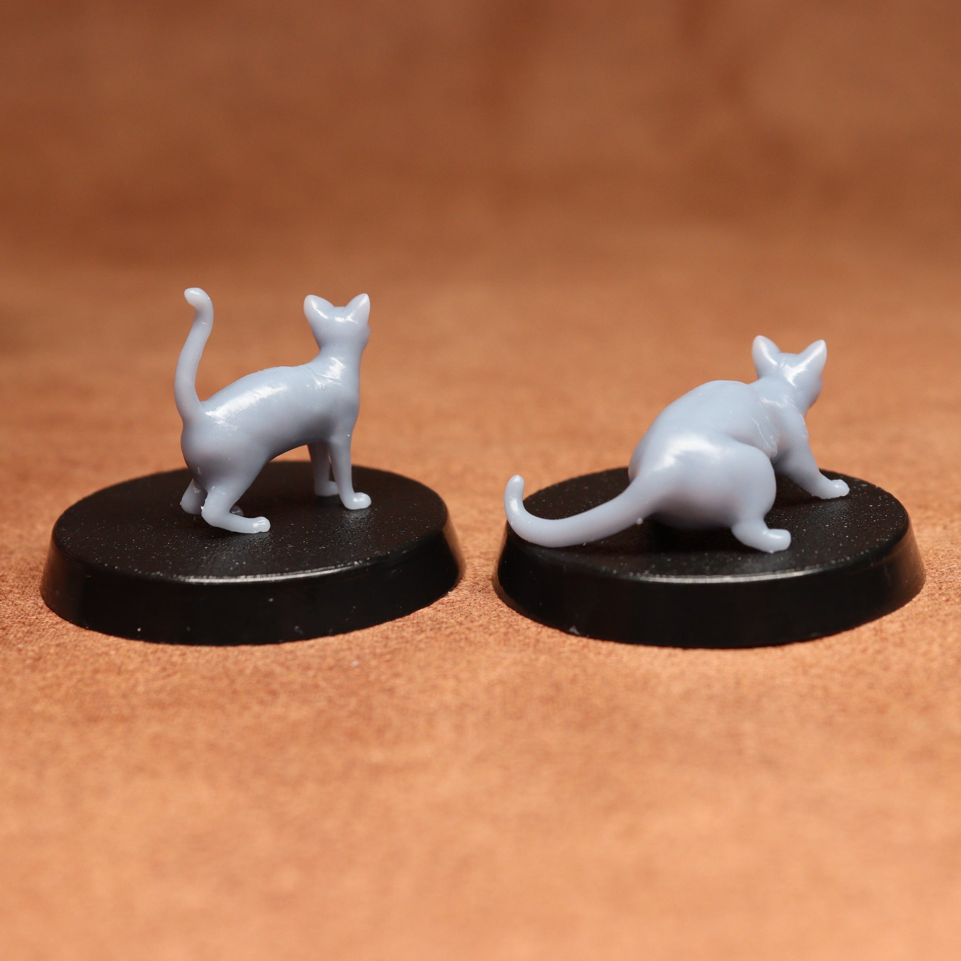 Two miniature cat figurines on black bases against a brown background