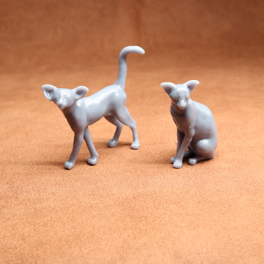 Two gray ceramic cat figurines on a brown surface