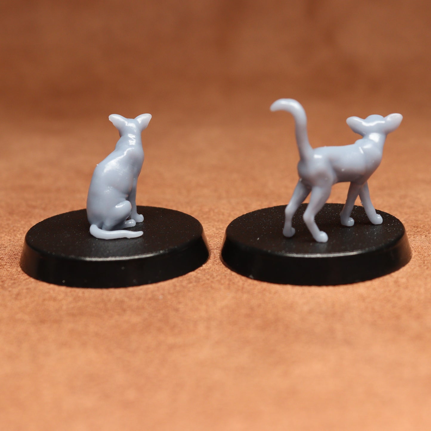 Two white cats figurines on black bases against a brown background
