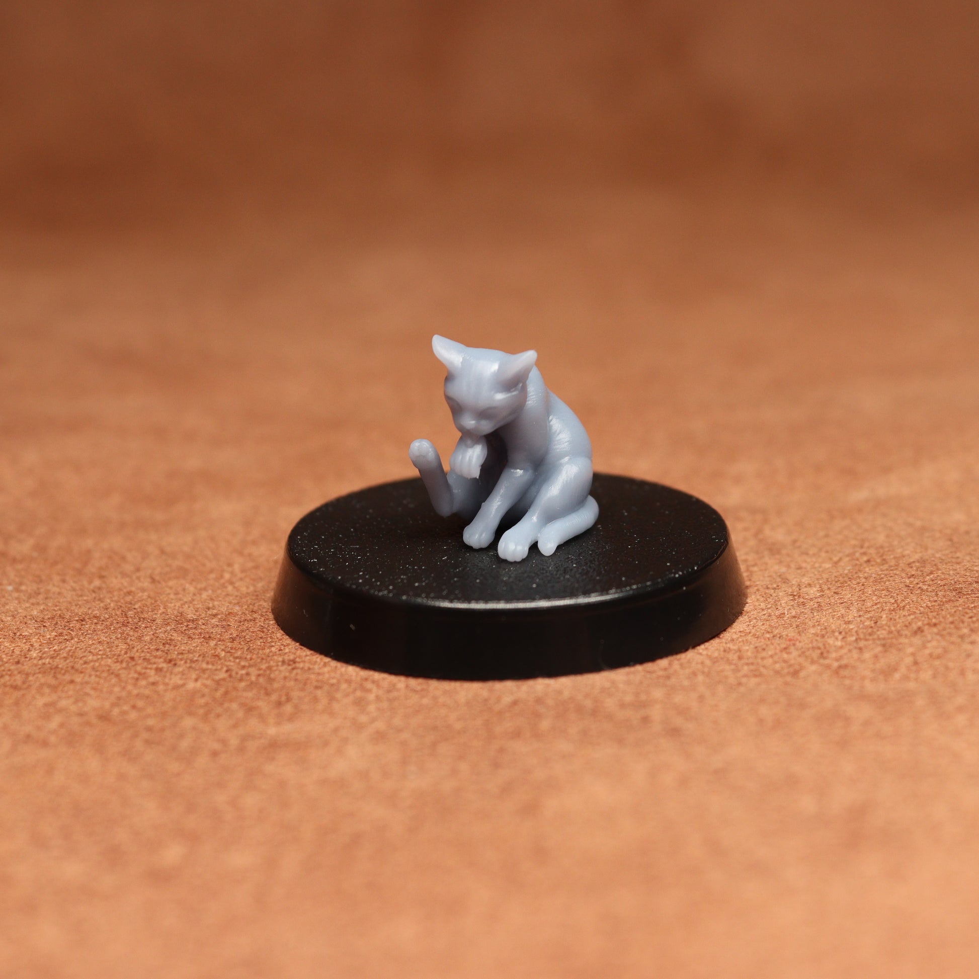 Small gray cat figurine on a black round base against a brown background