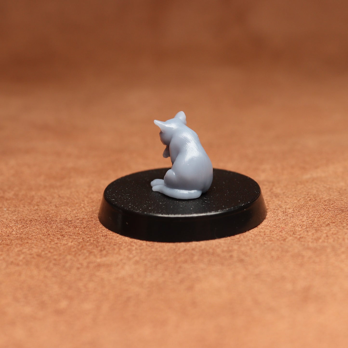 Small gray cat figurine on a black round base against a brown background