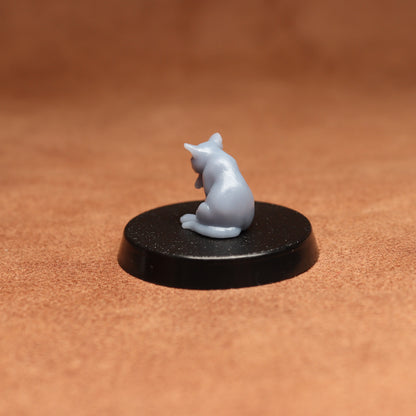 Small gray cat figurine on a black round base against a brown background