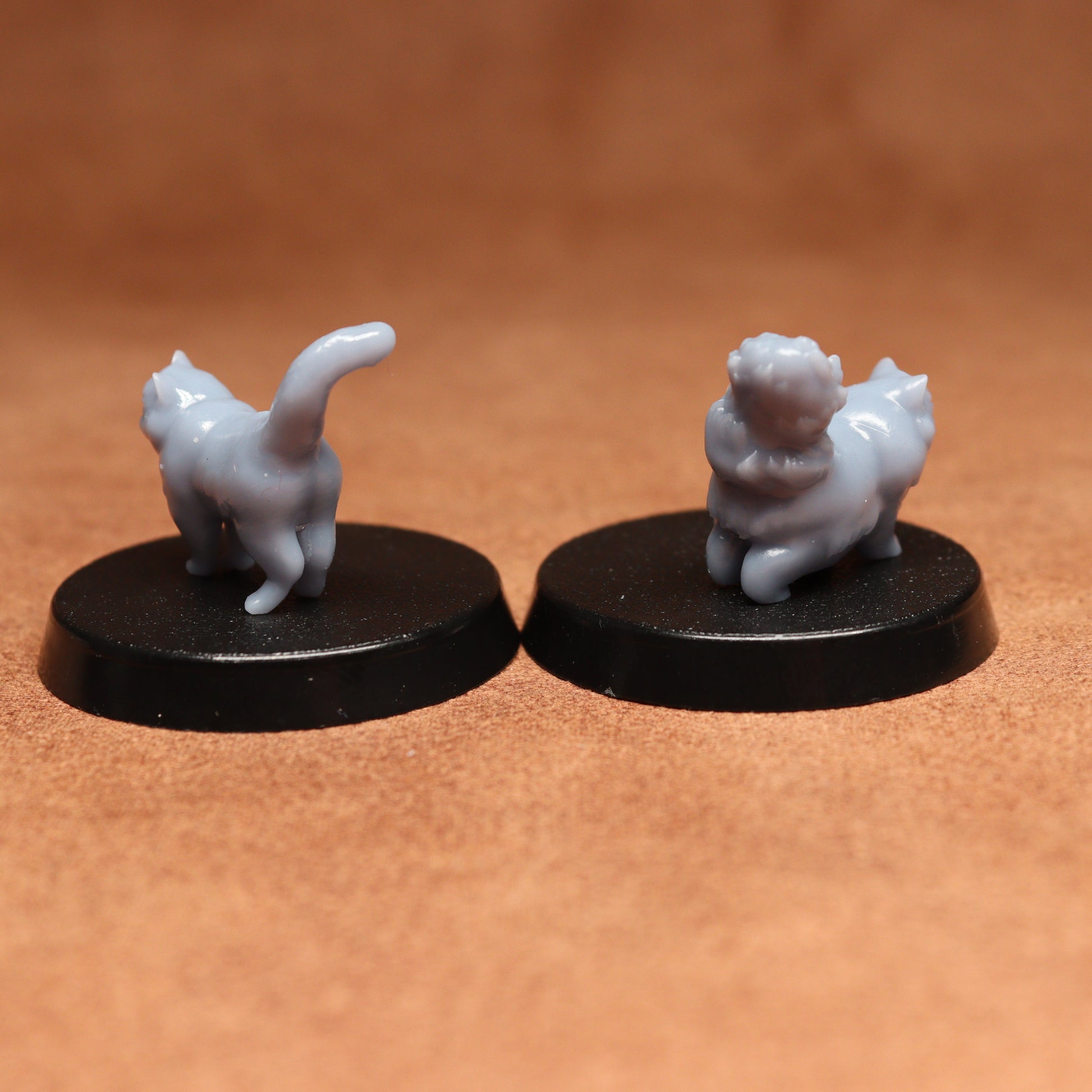 Two miniature cat figurines on black bases against a brown background
