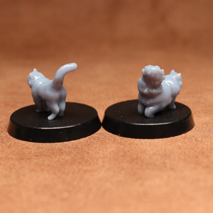 Two miniature cat figurines on black bases against a brown background