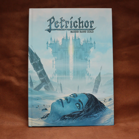 A hardcover book titled 'Petrichor: Blood RunsCold' featuring fantasy cover art of a snowy landscape, a large castle, and a blue-toned face in the foreground, photographed on a brown fabric background.