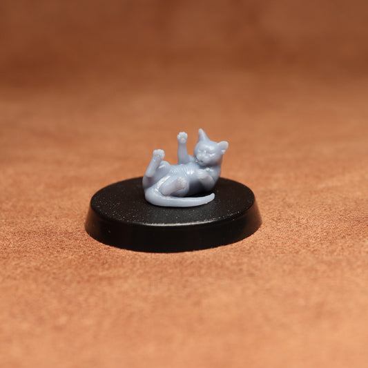 a grey cat figurine laying on its back on a black base on a brown background